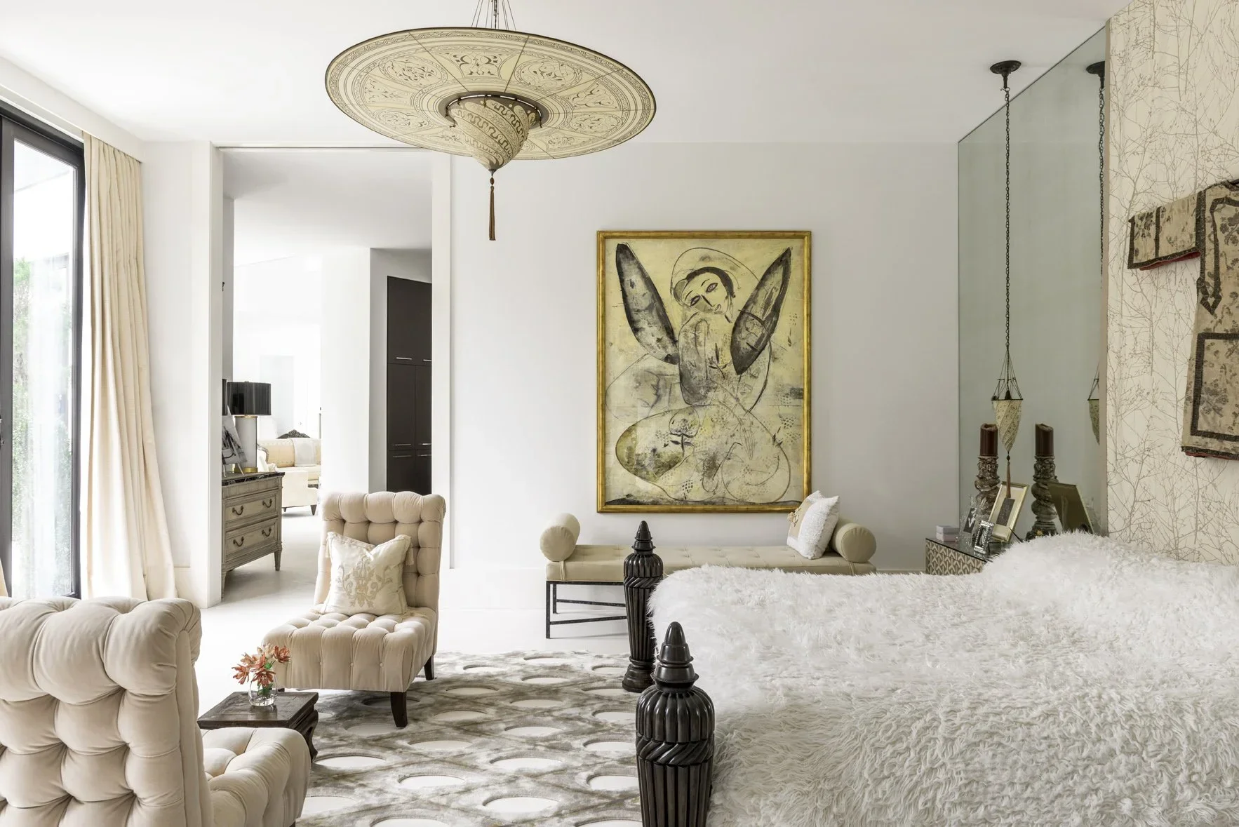 Living room with cream-colored furniture, large paintings, decorative candles, and a large glass door with curtains.